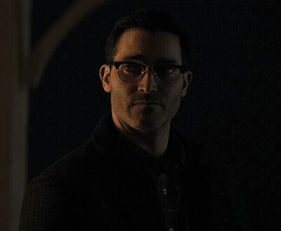 A Man Wearing Glasses And A Black Jacket Stands In The Dark GIF