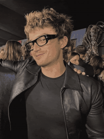 A Man Wearing Glasses And A Black Leather Jacket Smiles GIF