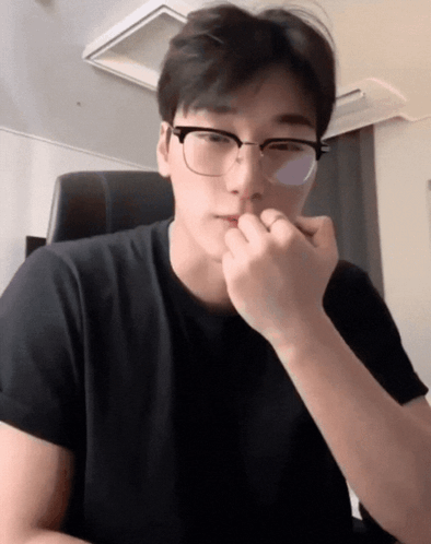 A Man Wearing Glasses And A Black Shirt Holds His Hand To His Chin GIF