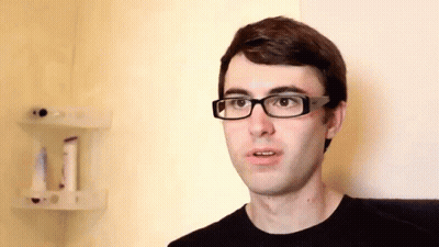 A Man Wearing Glasses And A Black Shirt Is Looking At The Camera GIF