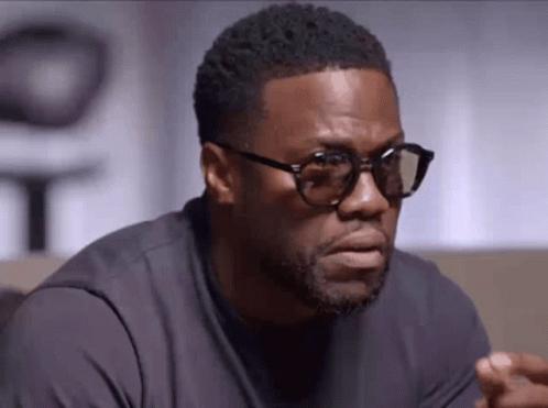A Man Wearing Glasses And A Black Shirt Is Looking At The Camera . GIF