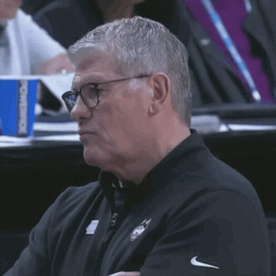 A Man Wearing Glasses And A Black Shirt Is Sitting In A Stadium Watching A Game GIF