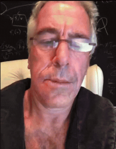 A Man Wearing Glasses And A Black Shirt Is Sitting In Front Of A Blackboard GIF