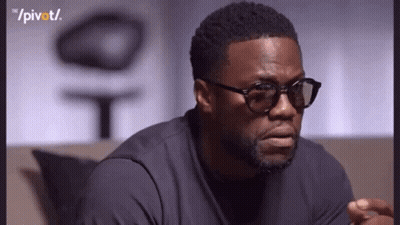 A Man Wearing Glasses And A Black Shirt Is Sitting On A Couch And Making A Funny Face . GIF