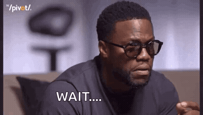 A Man Wearing Glasses And A Black Shirt Is Sitting On A Couch And Saying `` Wait ... '' . GIF