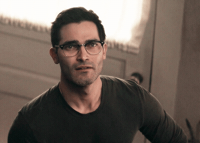 A Man Wearing Glasses And A Black Shirt Is Standing In Front Of A Door GIF