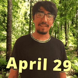 A Man Wearing Glasses And A Black Shirt Stands In The Woods On April 29 GIF