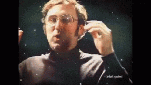 A Man Wearing Glasses And A Black Turtleneck Is Holding A Pair Of Headphones In His Hand . GIF