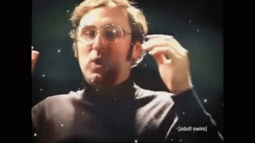 A Man Wearing Glasses And A Black Turtleneck Is Holding A Pair Of Headphones . GIF
