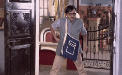 A Man Wearing Glasses And A Blue Bag Is Standing In Front Of A Black Door GIF