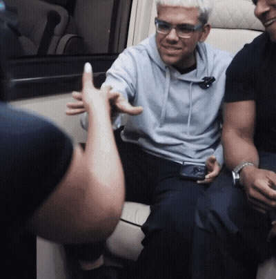 A Man Wearing Glasses And A Blue Hoodie Is Sitting In A Chair GIF