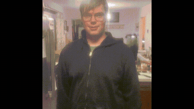 A Man Wearing Glasses And A Blue Jacket Stands In Front Of A Refrigerator GIF