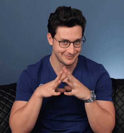 A Man Wearing Glasses And A Blue Shirt Has His Hands Folded In A Triangle GIF