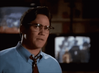 A Man Wearing Glasses And A Blue Shirt Is Looking At Something GIF