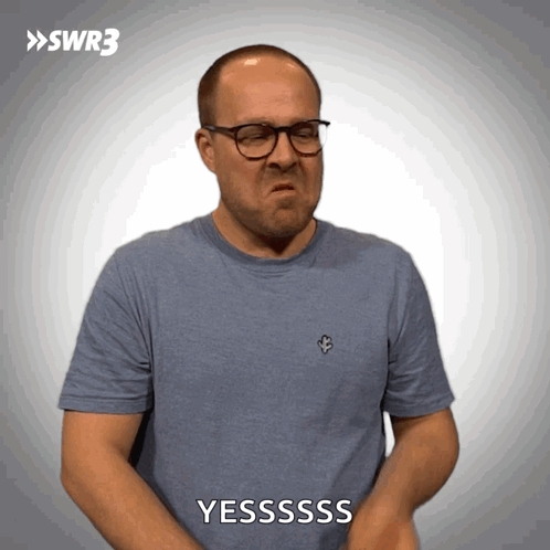 A Man Wearing Glasses And A Blue Shirt Is Making A Face And Says Yesssss GIF