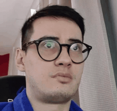 A Man Wearing Glasses And A Blue Shirt Is Making A Face GIF