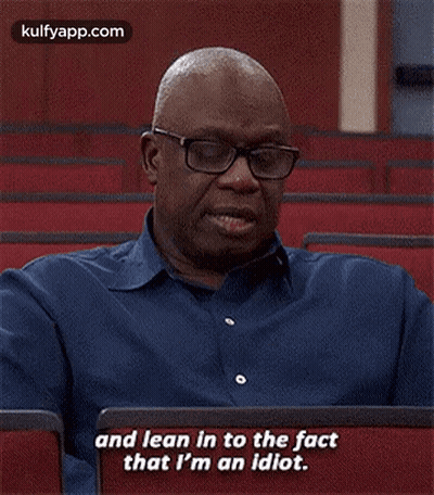 A Man Wearing Glasses And A Blue Shirt Is Sitting In A Lecture Hall . GIF