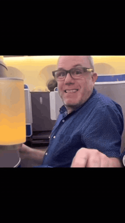 A Man Wearing Glasses And A Blue Shirt Is Smiling And Holding A Cup GIF