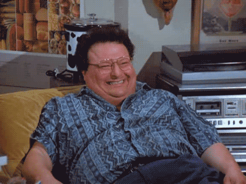 A Man Wearing Glasses And A Blue Shirt Is Smiling In Front Of A Record Player GIF