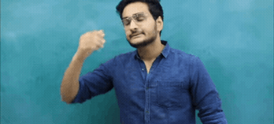 A Man Wearing Glasses And A Blue Shirt Is Standing In Front Of A Blue Wall And Making A Funny Face . GIF