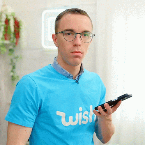 A Man Wearing Glasses And A Blue Shirt That Says Wish Holds A Cell Phone GIF