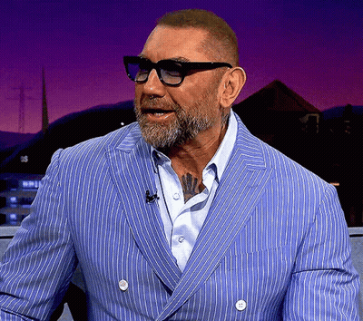 A Man Wearing Glasses And A Blue Striped Suit Has A Tattoo On His Chest GIF