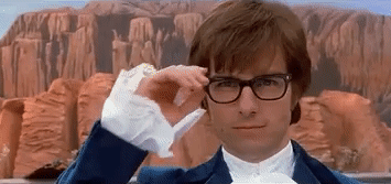 A Man Wearing Glasses And A Blue Suit Is Adjusting His Glasses In Front Of A Mountain . GIF