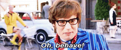 A Man Wearing Glasses And A Blue Suit Is Standing On A Street And Says `` Oh , Behave ! '' GIF