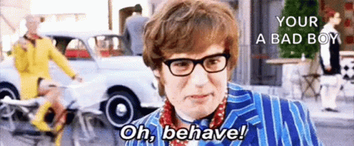 A Man Wearing Glasses And A Blue Suit Is Standing On A Street With A Car In The Background . GIF
