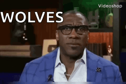 A Man Wearing Glasses And A Blue Suit Is Talking Into A Microphone And Says Wolves . GIF