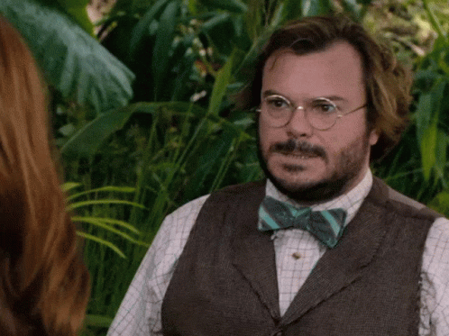 A Man Wearing Glasses And A Bow Tie Stands In The Jungle GIF