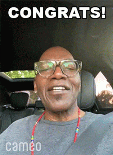 A Man Wearing Glasses And A Cameo Necklace Is Smiling GIF