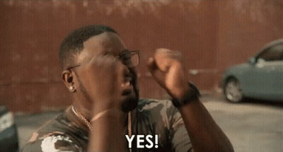 A Man Wearing Glasses And A Camouflage Shirt Is Holding His Fist Up And Saying Yes . GIF