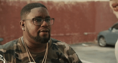 A Man Wearing Glasses And A Camouflage Shirt Is Standing In A Parking Lot . GIF