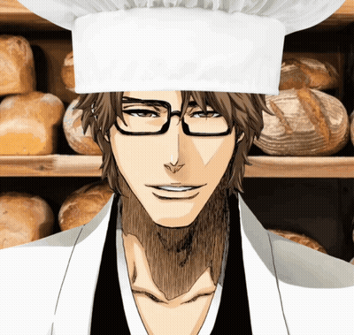 A Man Wearing Glasses And A Chef 'S Hat Is Smiling In Front Of A Shelf Of Bread GIF