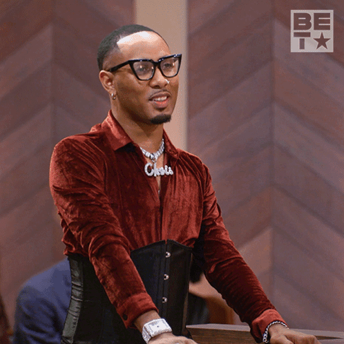 A Man Wearing Glasses And A Corset With The Word Chola On His Shirt GIF