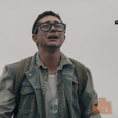 A Man Wearing Glasses And A Denim Jacket With The Long Walk Written On It GIF
