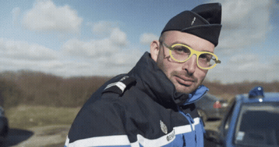A Man Wearing Glasses And A Gendarmerie Uniform Looks At The Camera GIF