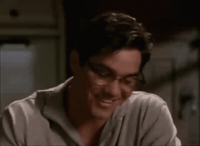 A Man Wearing Glasses And A Gray Shirt Smiles GIF