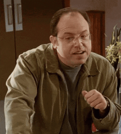 A Man Wearing Glasses And A Green Jacket Is Pointing At Something . GIF