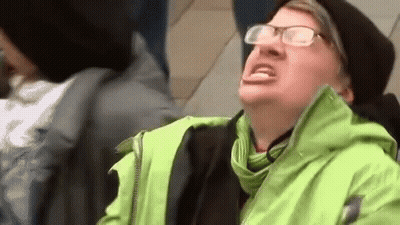 A Man Wearing Glasses And A Green Jacket Is Sitting On A Train . GIF