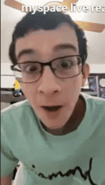 A Man Wearing Glasses And A Green Shirt Is Looking At The Camera . GIF