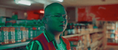 A Man Wearing Glasses And A Green Vest Is In A Store GIF