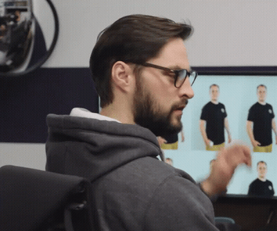 A Man Wearing Glasses And A Grey Hoodie Looks At A Monitor GIF