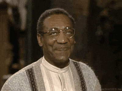 A Man Wearing Glasses And A Grey Sweater Is Smiling GIF