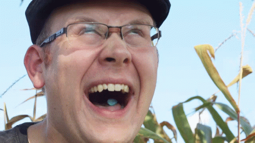 A Man Wearing Glasses And A Hat Is Laughing GIF