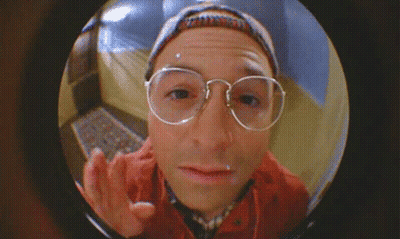 A Man Wearing Glasses And A Hat Is Looking Through A Door GIF