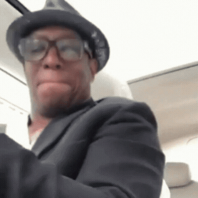 A Man Wearing Glasses And A Hat Is Making A Funny Face . GIF