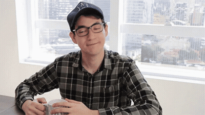 A Man Wearing Glasses And A Hat Is Sitting At A Table GIF
