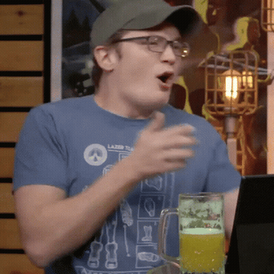 A Man Wearing Glasses And A Hat Is Sitting At A Table With A Glass Of Beer . GIF